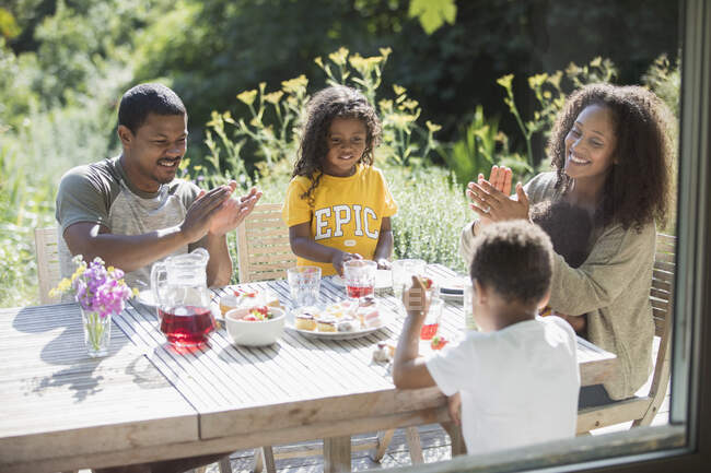 Happy family clapping and eating at sunny summer patio table — Stock Photo