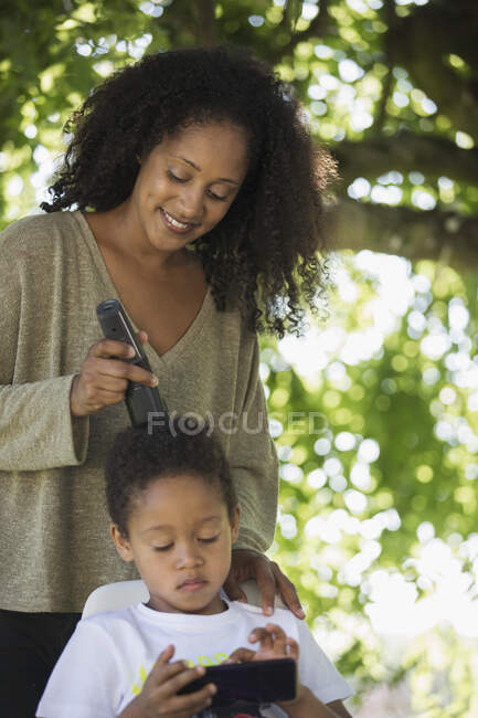 Mère coupe les cheveux de son fils sous l'arbre dans la cour arrière — Photo de stock