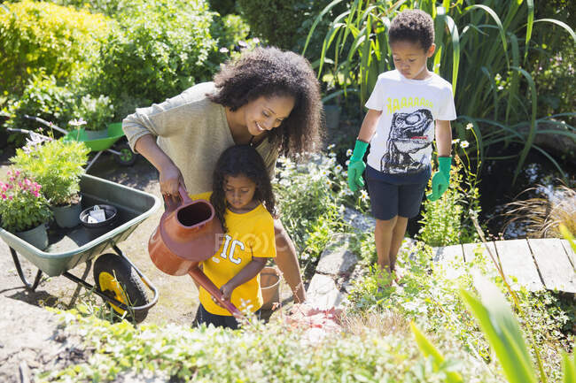 Mãe feliz e crianças que molham plantas no jardim ensolarado do verão — Fotografia de Stock
