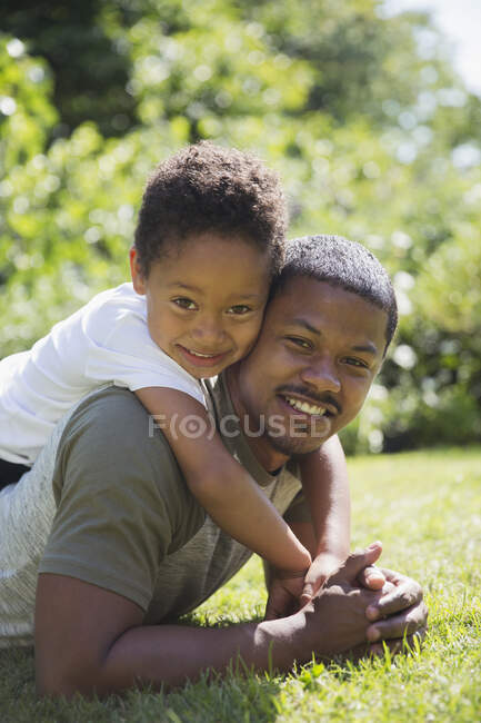 Ritratto felice padre e figlio che si abbracciano nella soleggiata erba estiva — Foto stock