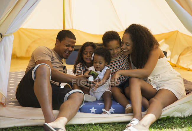 Happy family using smart phone inside tent — Stock Photo