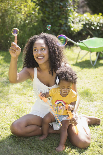 Happy mother and toddler daughter blowing bubbles in sunny grass — Stock Photo