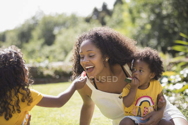 Daughter feeding watermelon to happy mother in sunny backyard — Stock Photo