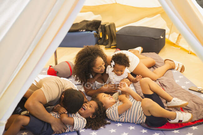 Família brincalhona fazendo cócegas e rindo dentro da tenda — Fotografia de Stock