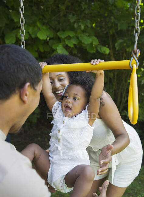 Батьки грають з дочкою малюка на гойдалці на задньому дворі — стокове фото