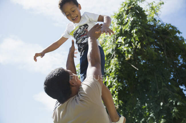 Father throwing son playfully overhead in sunshine — Stock Photo
