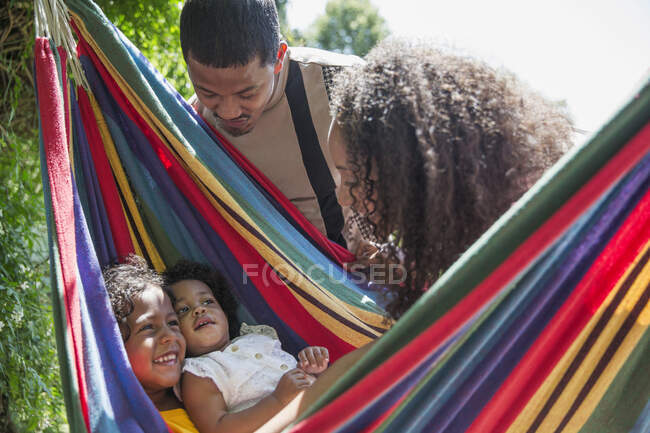 Родители смотрят на счастливых дочерей в солнечном летнем гамаке — стоковое фото