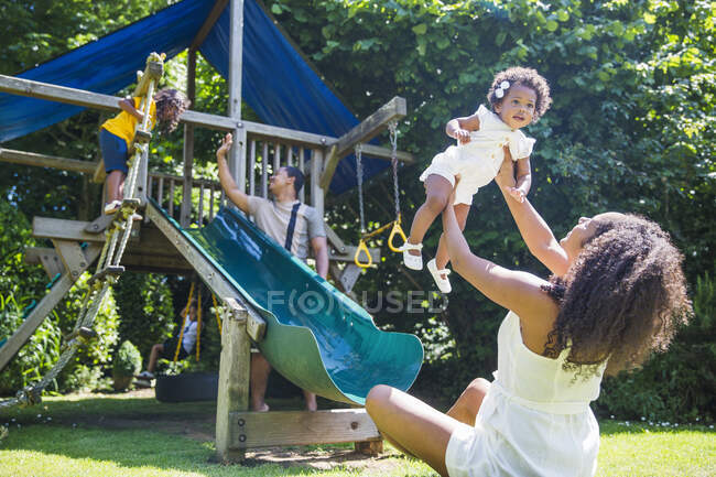 Familia feliz jugando en el patio de recreo situado en el soleado patio trasero de verano - foto de stock