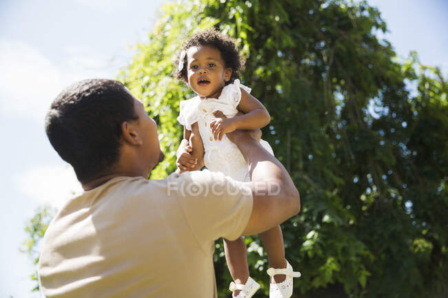 Pai levantando criança filha sobrecarga no jardim de verão ensolarado — Fotografia de Stock
