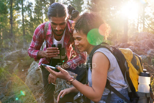 Felice giovane coppia escursionistica utilizzando smart phone in boschi soleggiati — Foto stock