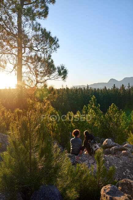 Joven pareja de senderismo relajándose en la roca en bosques pintorescos soleados - foto de stock