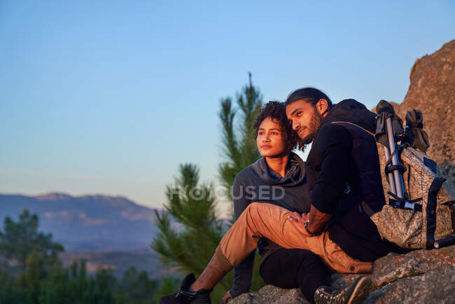 Serena joven pareja de senderismo disfrutando de la puesta del sol en las rocas - foto de stock