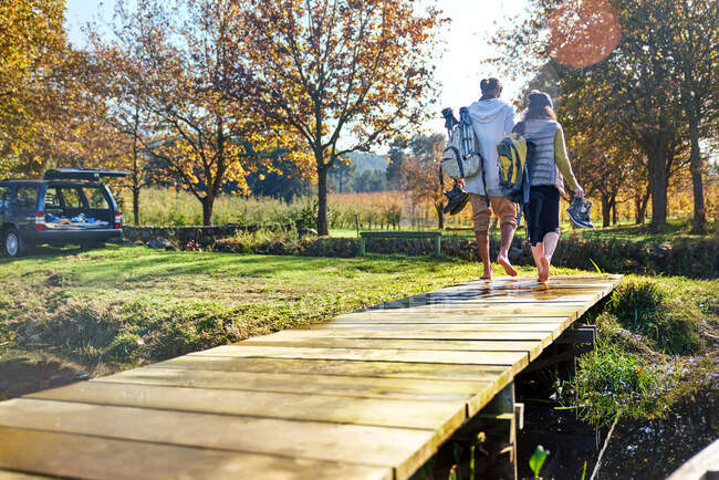 Barefoot young couple walking on sunny autumn lakeside dock — Stock Photo