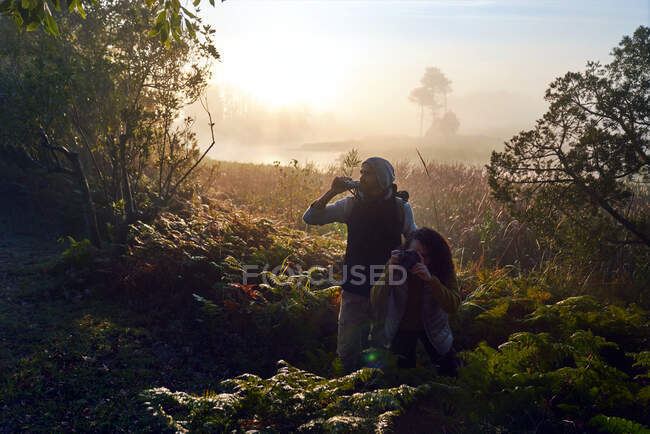 Curioso jovem casal caminhadas com binóculos e câmera em bosques ensolarados — Fotografia de Stock