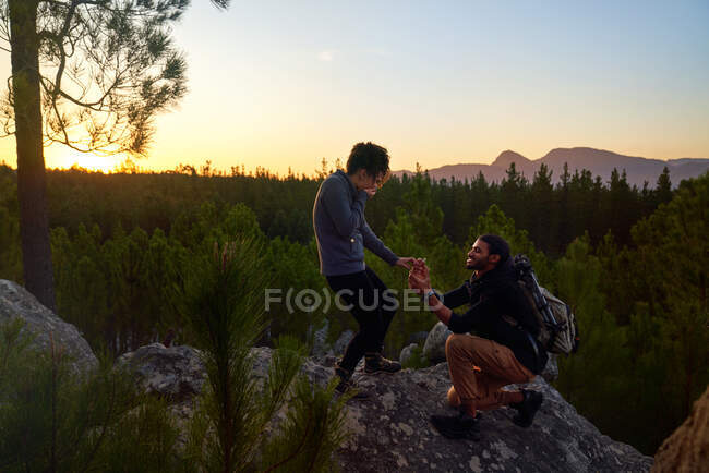 Jeune homme avec bague de fiançailles demandant une femme sur le rocher au coucher du soleil — Photo de stock