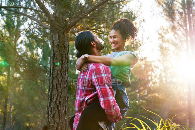 Affectionate young man holding happy girlfriend in sunny woods — Stock Photo