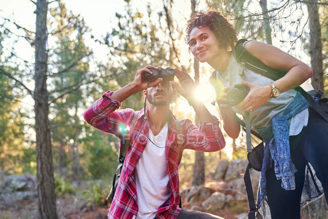Curious young hiker couple using binoculars and camera in sunny woods — Stock Photo