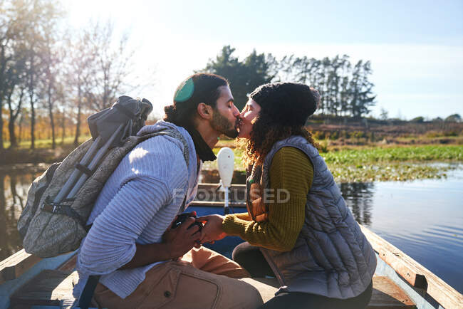 Casal jovem afetuoso beijando em barco a remos no lago de outono ensolarado — Fotografia de Stock