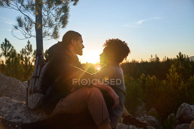 Cariñosa joven pareja de senderismo disfrutando de la tranquila puesta de sol en los bosques - foto de stock