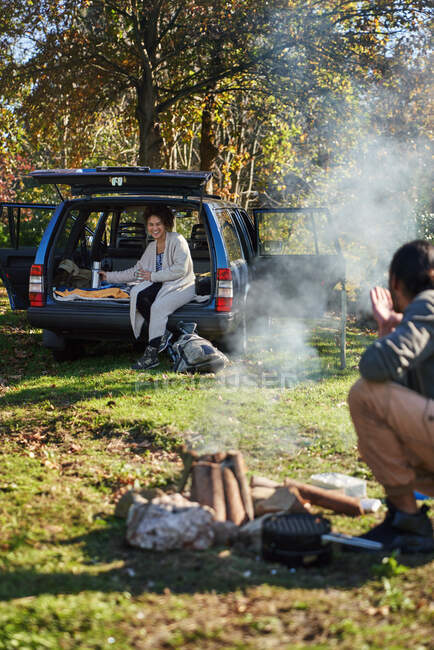 Young couple camping out of car and starting campfire in field — Stock Photo