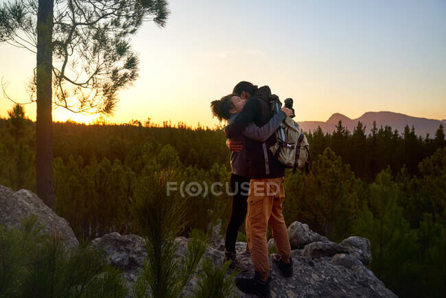 Affectionate young hiker couple hiking on rock in sunset woods — Stock Photo