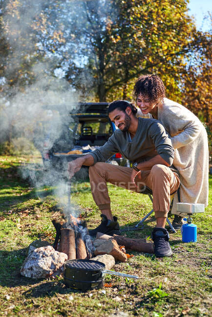 Happy young couple enjoying campfire in sunny autumn field — Stock Photo