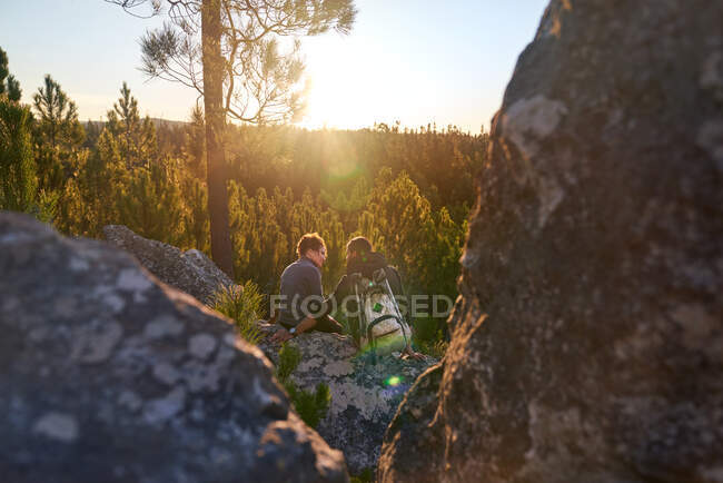 Cariñosa pareja joven excursionista relajarse en la roca en los bosques soleados atardecer - foto de stock
