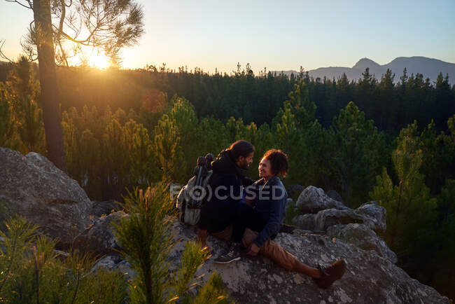 Feliz casal jovem afetuoso relaxando em rochas na floresta ao pôr do sol — Fotografia de Stock