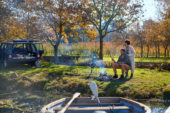 Happy young couple fishing at sunny autumn riverside — Stock Photo