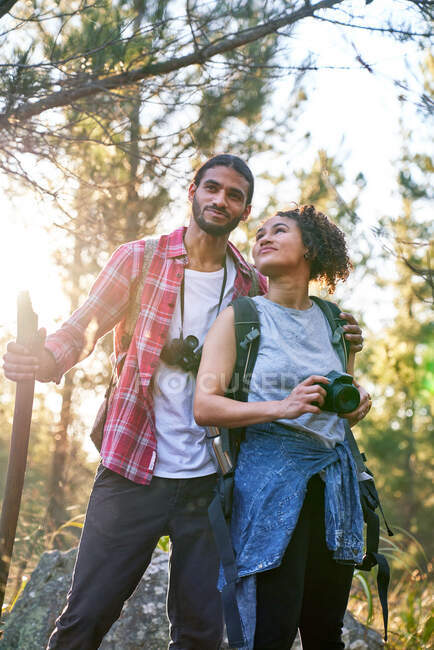 Feliz joven pareja de senderismo con cámara y prismáticos en bosques soleados - foto de stock