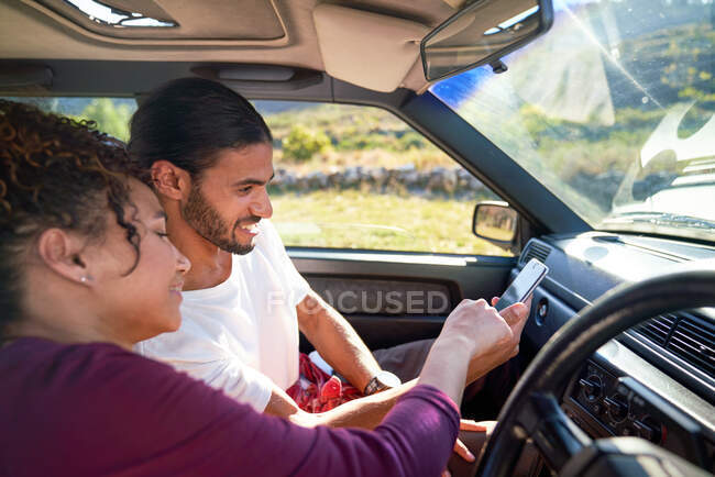 Jeune couple utilisant un téléphone intelligent sur la route en voiture ensoleillée — Photo de stock