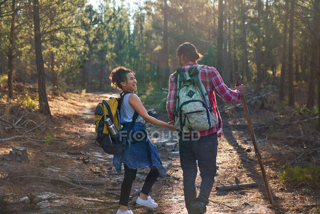 Happy young couple with backpacks hiking in sunny woods — Stock Photo