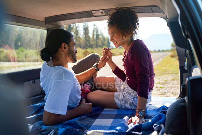 Heureux couple affectueux jeune tenant la main à l'arrière de la voiture ensoleillée — Photo de stock