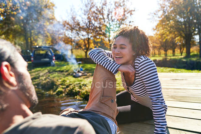 Feliz joven pareja relajándose en el soleado muelle de otoño - foto de stock