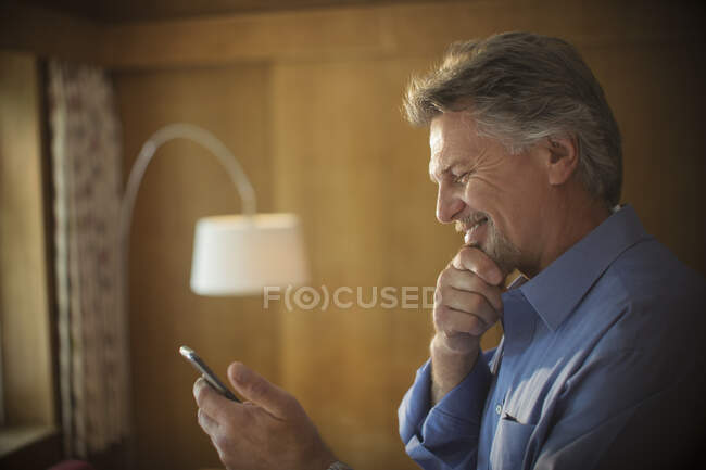 Hombre mayor sonriente usando un teléfono inteligente en casa - foto de stock