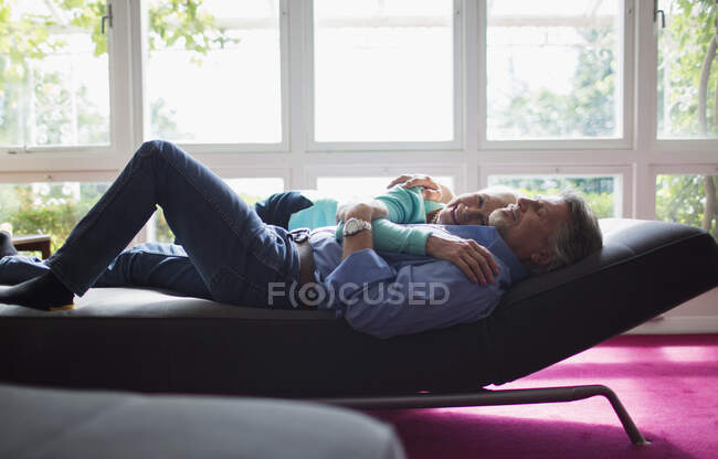 Cariñosa pareja abrazándose en el sillón en la ventana soleada - foto de stock