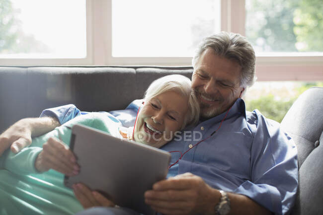 Felice coppia anziana condivisione cuffie e tablet digitale sul divano — Foto stock