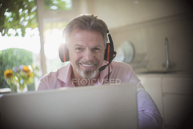 Портрет усміхненого старшого чоловіка з навушниками, що працюють на ноутбуці — стокове фото
