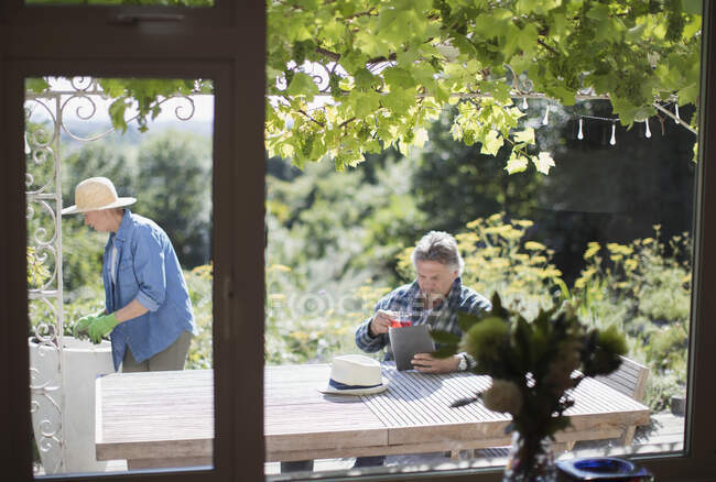 Seniorenpaar gärtnert und nutzt digitales Tablet auf sonniger Sommerterrasse — Stockfoto