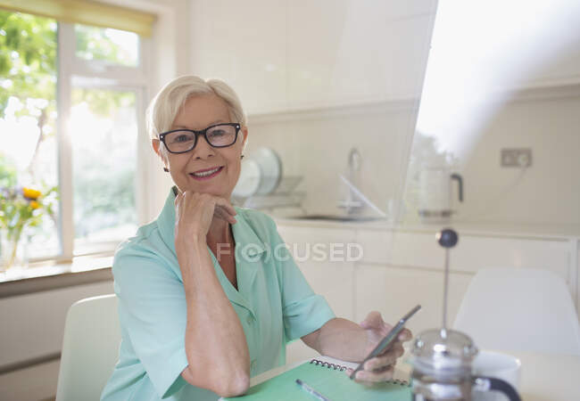 Portrait femme âgée confiante en utilisant le téléphone intelligent dans la cuisine du matin — Photo de stock