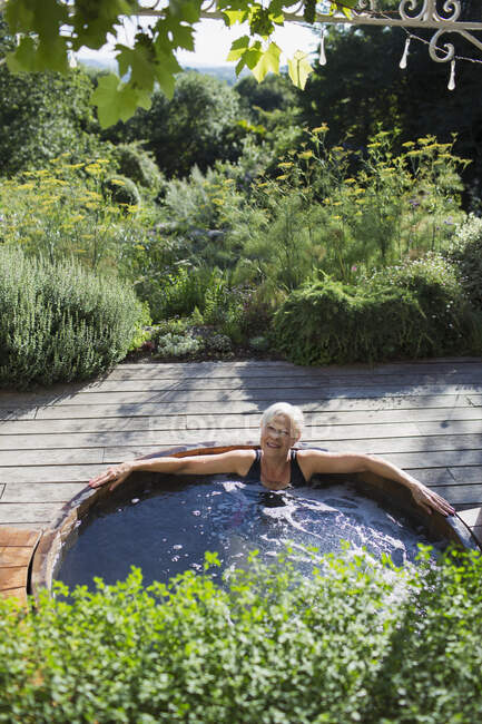 Portrait femme âgée insouciante se détendre dans un bain à remous sur terrasse ensoleillée — Photo de stock