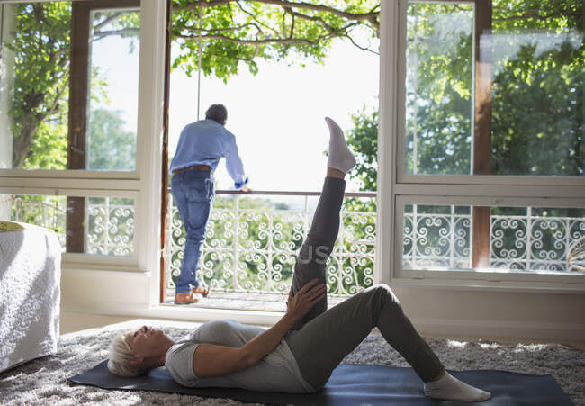 Seniorin dehnt sich an Sommerbalkontür auf Yogamatte — Stockfoto