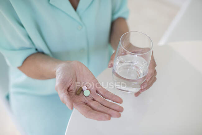 Старшая женщина принимает витамины с водой — стоковое фото