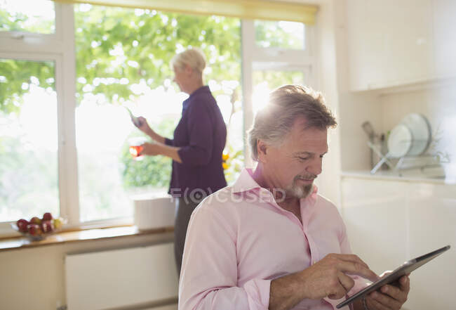 Homem sênior usando tablet digital na cozinha da manhã ensolarada — Fotografia de Stock
