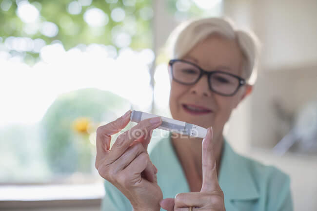 Старша жінка з діабетом за допомогою лічильника глюкози в крові на пальці — стокове фото