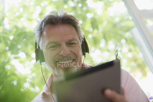 Смолящий пожилой человек слушает музыку в наушниках и цифровом планшете — стоковое фото