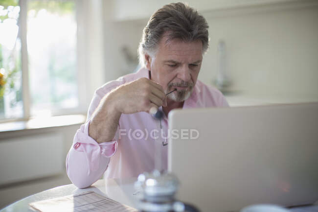 Homme âgé travaillant à l'ordinateur portable à la table de cuisine — Photo de stock