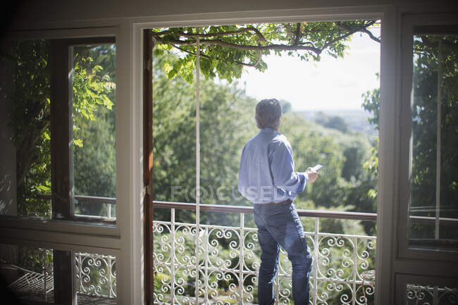 Uomo anziano utilizzando smart phone su soleggiato tranquillo balcone estivo — Foto stock