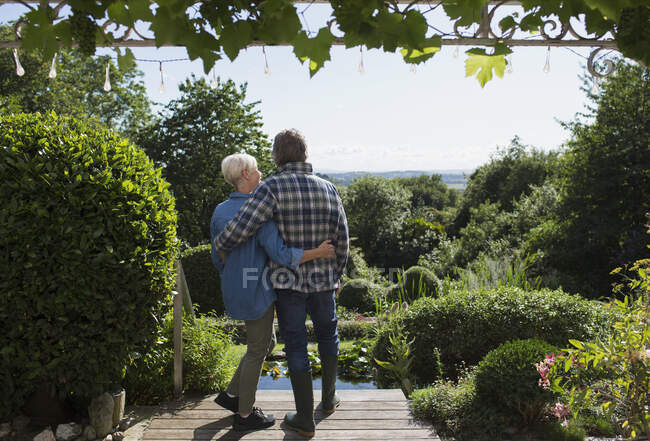 Cariñosa pareja de ancianos abrazándose en el soleado patio del jardín de verano - foto de stock