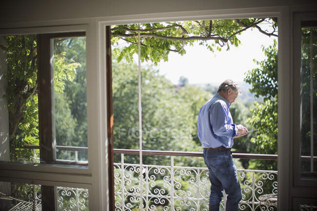 Senior nutzt digitales Tablet auf sonnigem idyllischen Balkon — Stockfoto